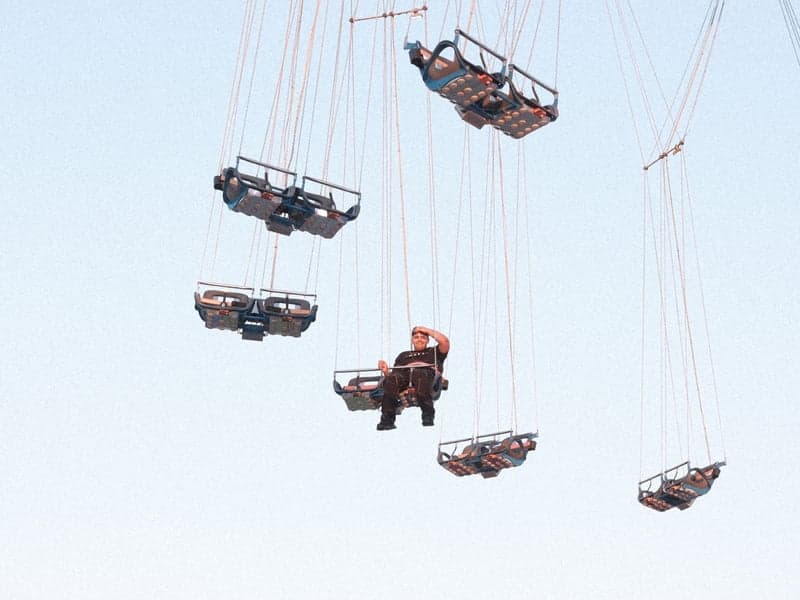 A person sitting in a suspended swing ride against a clear blue sky.