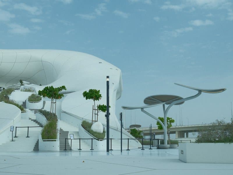 Modern architectural structure with white curves and green trees under a cloudy sky.