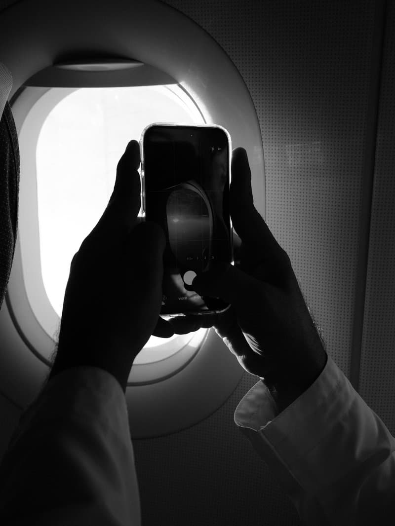 Silhouette of hands holding a smartphone near an airplane window, capturing light.