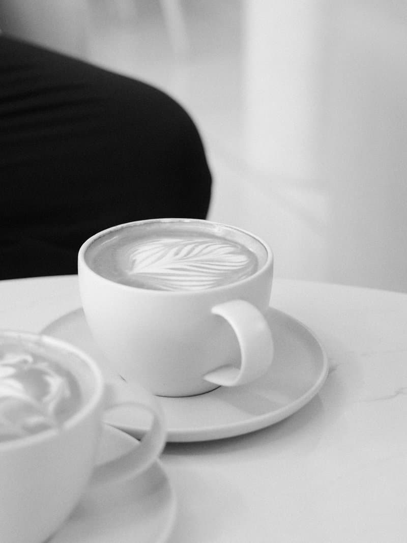 Two cups of coffee on a white table, one with latte art, in a minimalist setting.