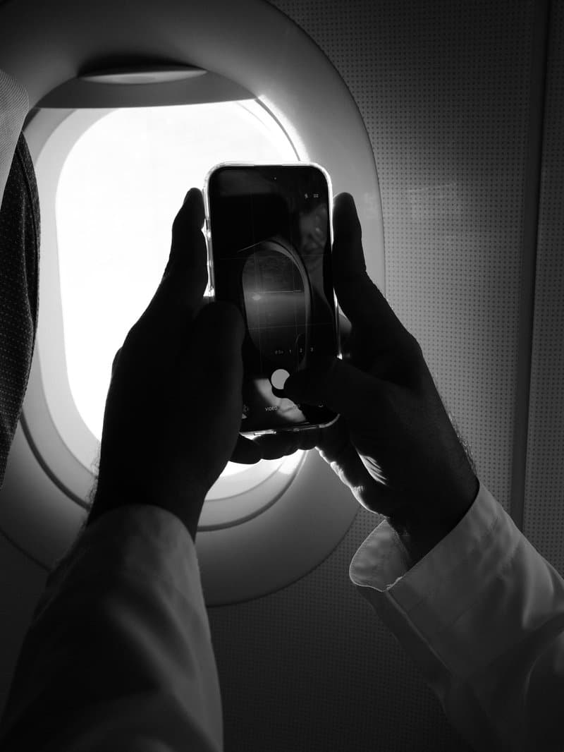 A person holding a smartphone up to an airplane window, capturing the view outside.