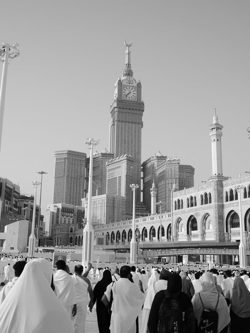 Crowd of people in white garments walking towards a tall building in a cityscape.