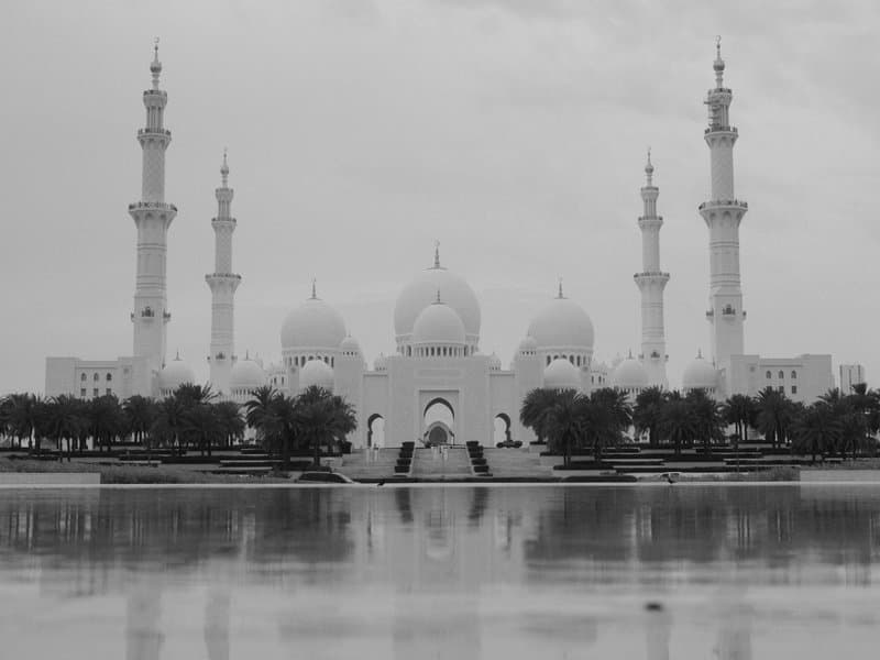 A grand mosque with multiple minarets and domes reflected in a calm water surface.