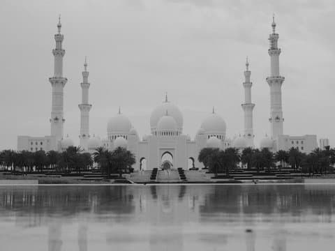 A grand mosque with multiple minarets and domes reflected in a calm water surface.