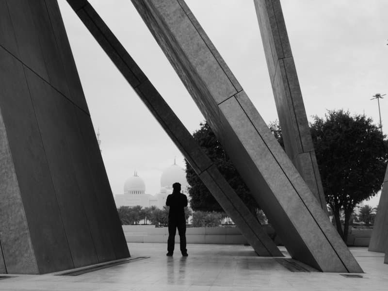 Silhouette of a person standing under large concrete structures with a dome in the background.