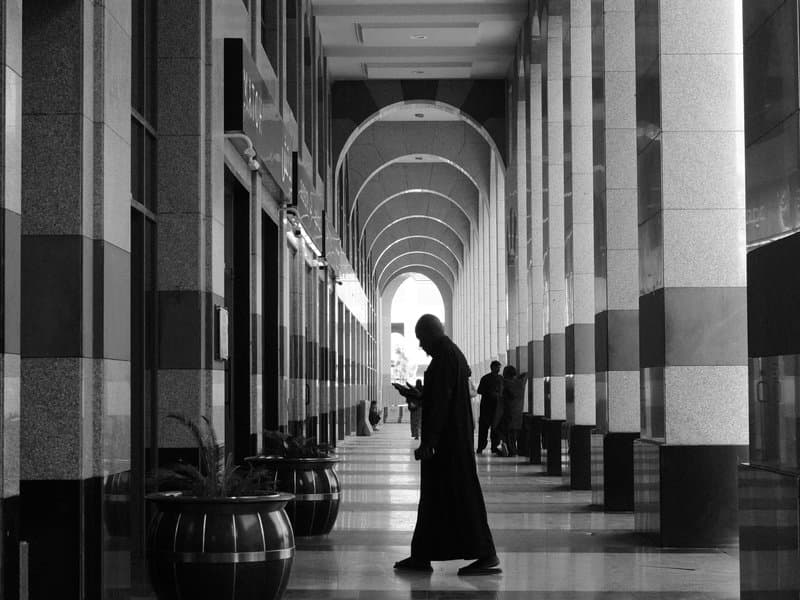 A silhouette of a monk walking through a corridor with arches, creating a serene atmosphere.