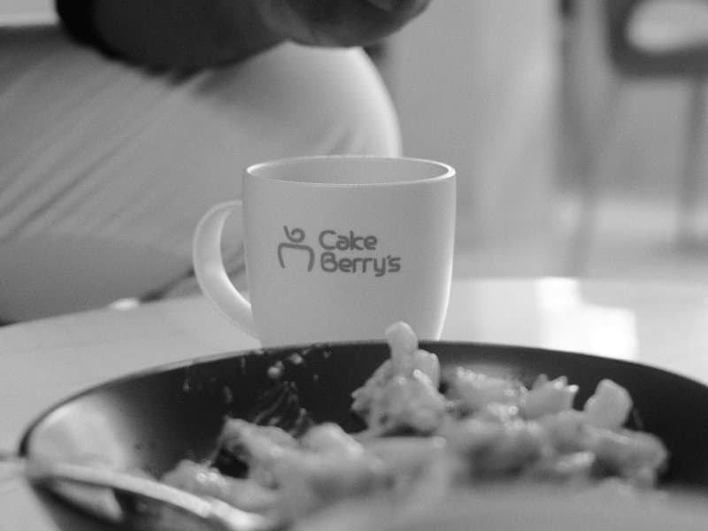 A close-up of a coffee cup and a plate of food on a table, with a blurred background.