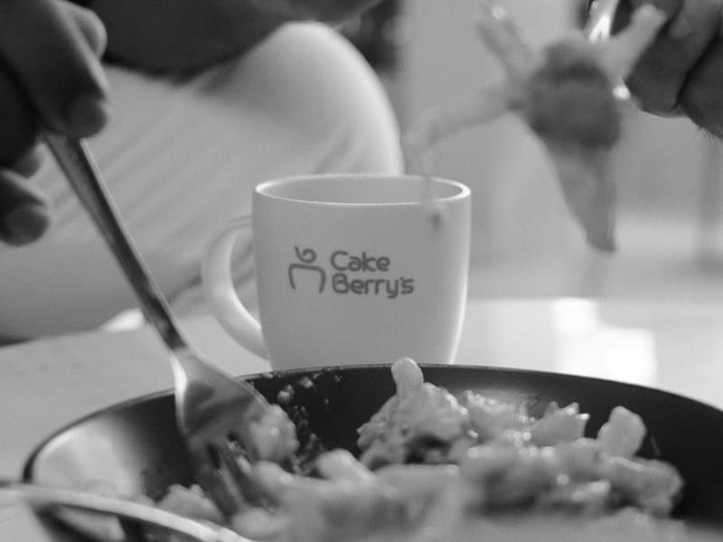 A close-up of hands holding utensils over a plate of food and a coffee cup with a logo.