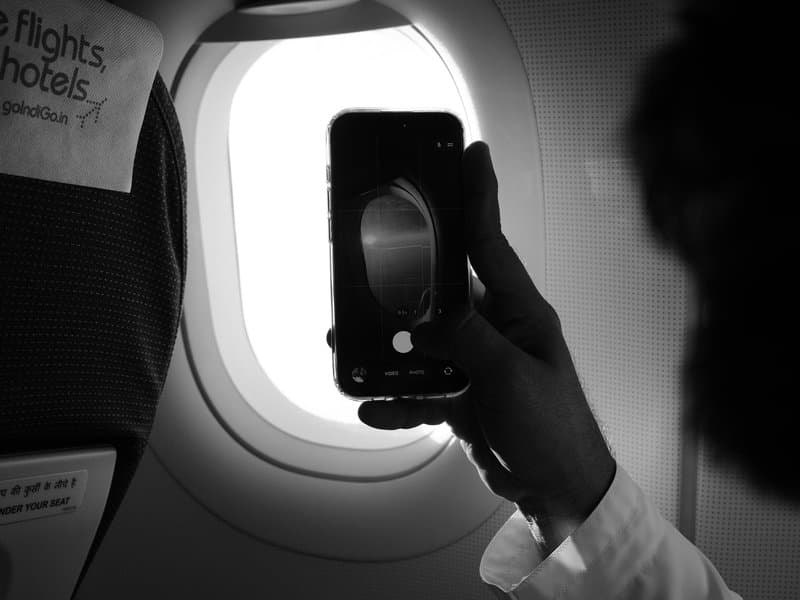 A hand holding a smartphone capturing an airplane window view, with a blurred seatback in the foreground.