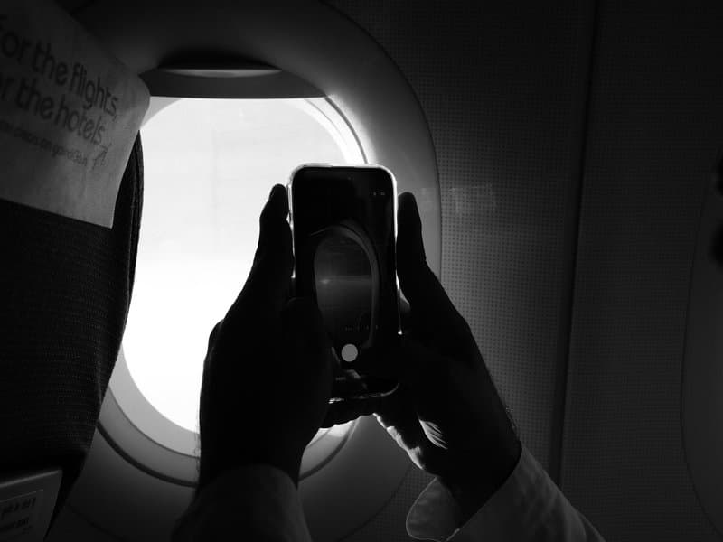 A silhouette of hands holding a smartphone near an airplane window, capturing the outside view.
