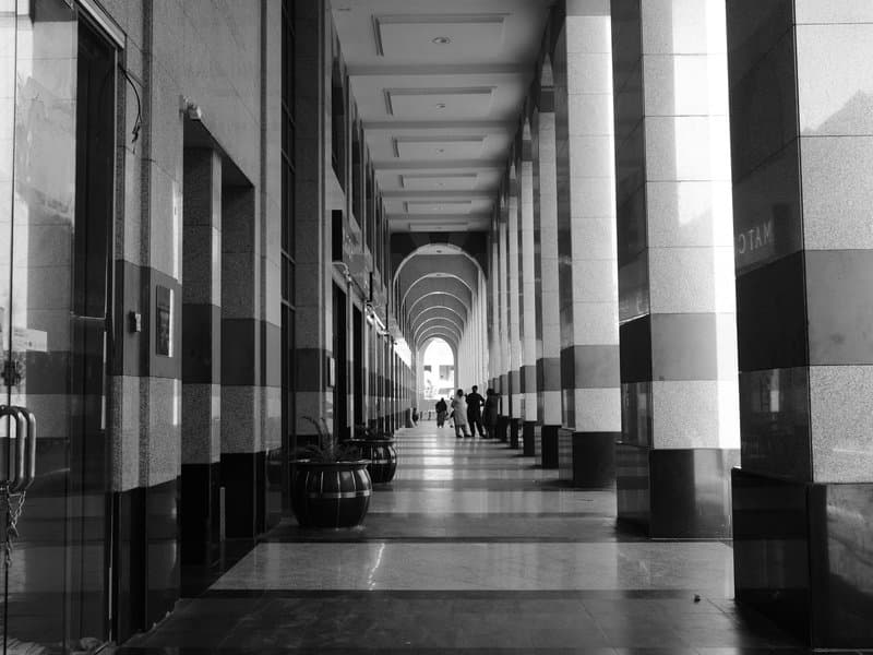 A long corridor with striped columns and arches, leading to a distant exit with people walking.