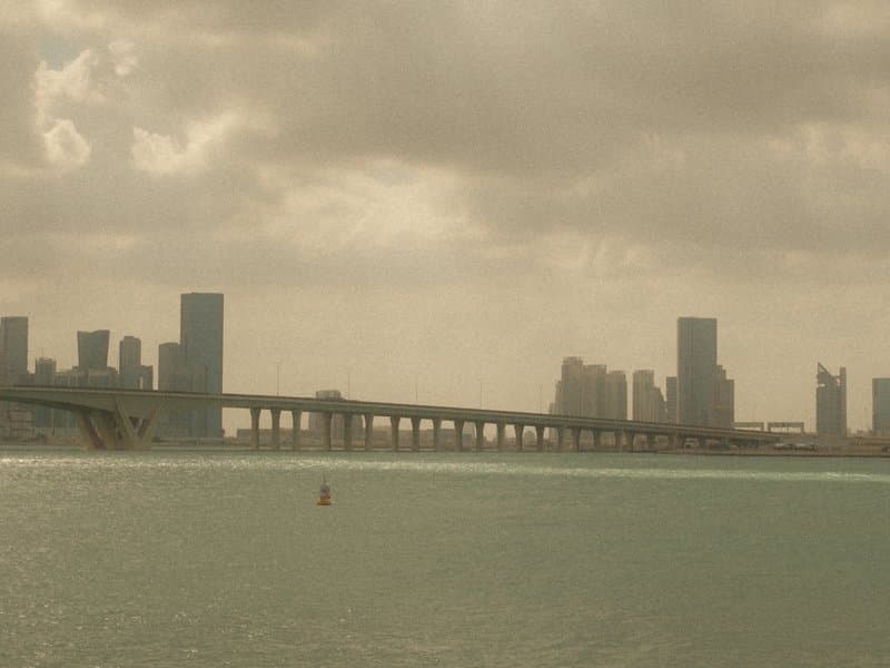 A hazy view of a city skyline with a bridge over water, under a cloudy sky.