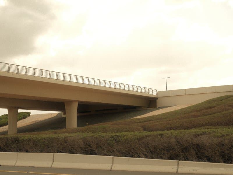 A low-angle view of an overpass with a cloudy sky in the background and green grass in the foreground.