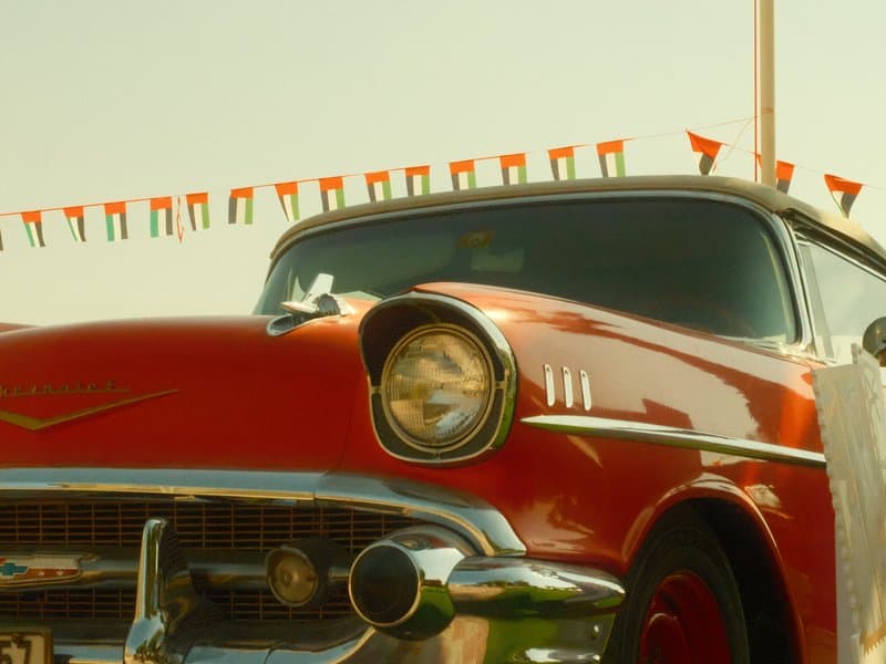 A vintage red car with a shiny chrome bumper parked under colorful flags against a clear sky.