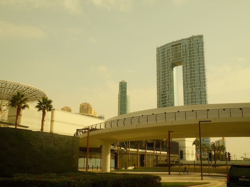 Urban scene featuring modern architecture with a distinctive building and palm trees under a hazy sky.