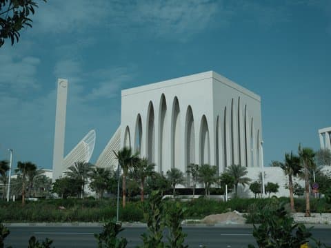 Modern architectural building with unique design against a blue sky, surrounded by palm trees.