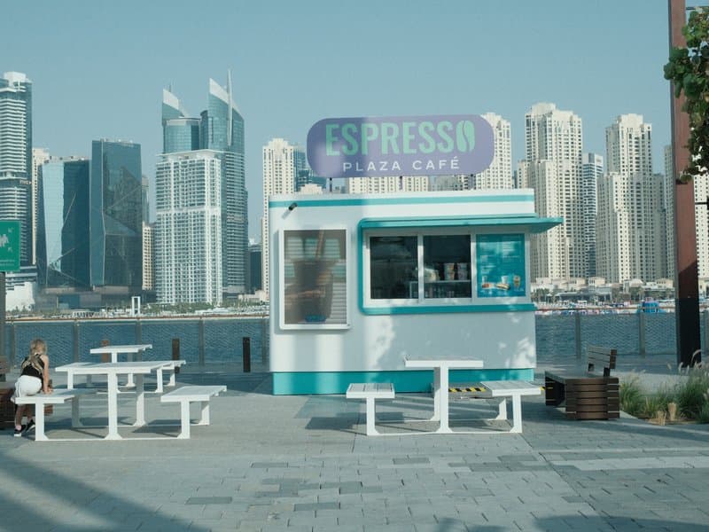 A small espresso kiosk by the waterfront with modern skyscrapers in the background.