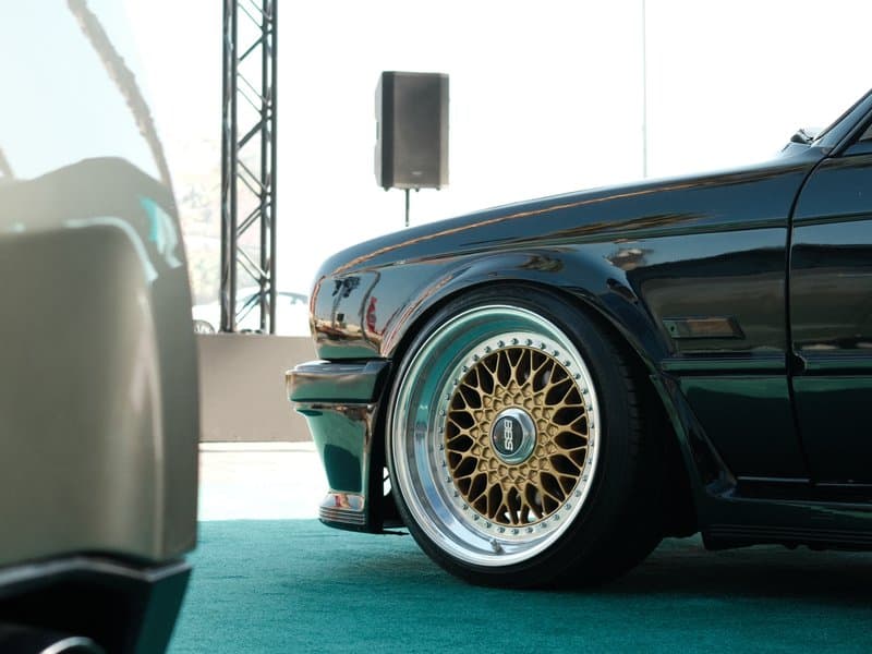 Close-up of a classic car's wheel and body, showcasing intricate gold rims and a sleek black finish.