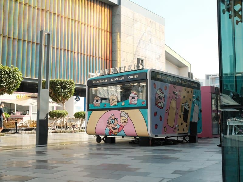 A colorful food truck parked in an urban setting with modern architecture in the background.