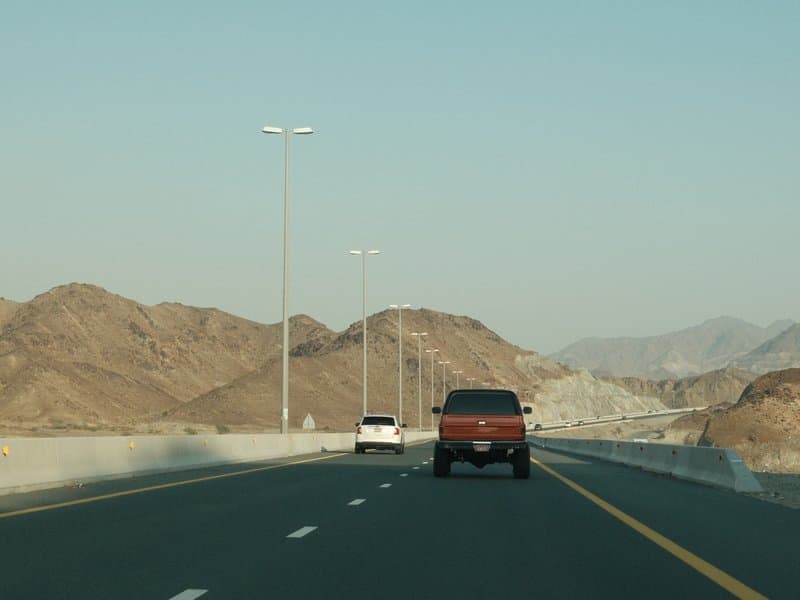 Two cars driving on a highway with mountains in the background under a clear sky.