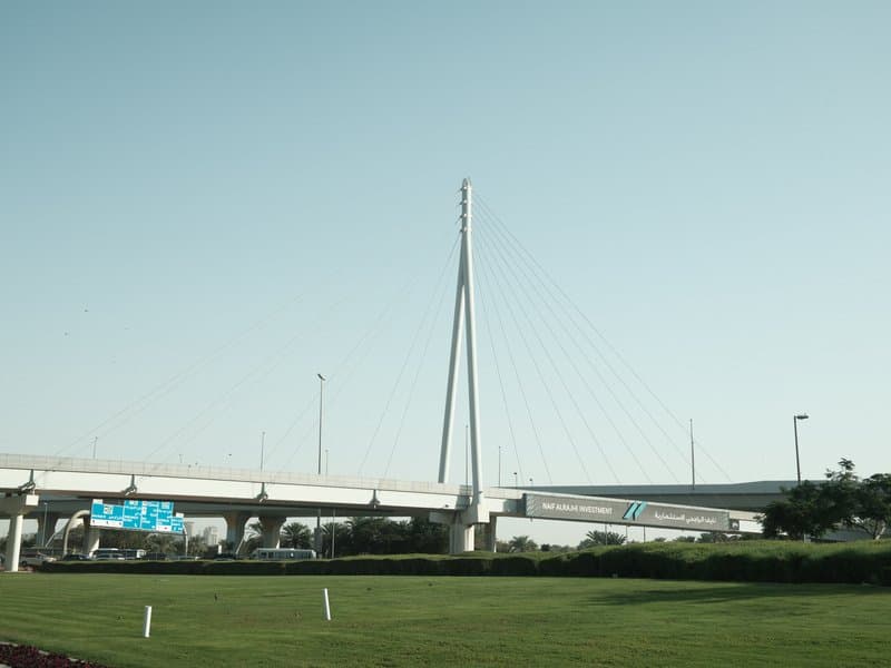 A modern cable-stayed bridge against a clear sky, with green grass in the foreground.