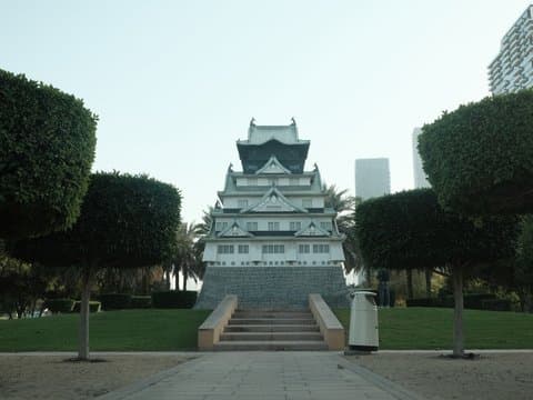 A traditional-style building with a tiered roof, surrounded by neatly trimmed bushes and palm trees.