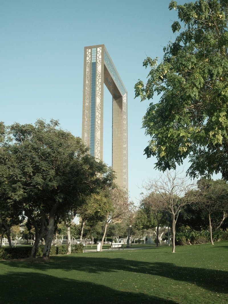 A tall architectural structure framed by trees in a park setting under clear skies.