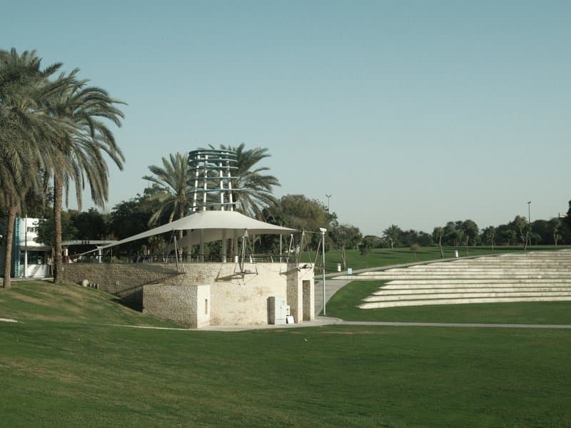 A modern amphitheater surrounded by palm trees and green grass under a clear sky.