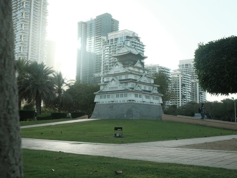 A modern building resembling a castle structure surrounded by greenery and urban skyscrapers.
