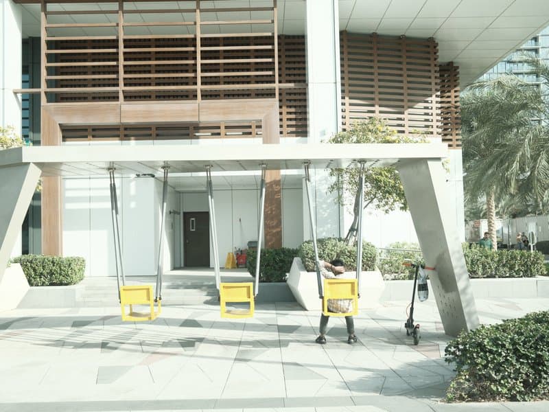 Two yellow swings under a modern building with a minimalist design and greenery around.