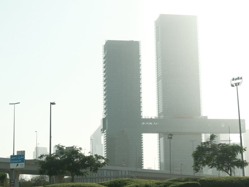 Two tall buildings shrouded in mist with a highway in the foreground.