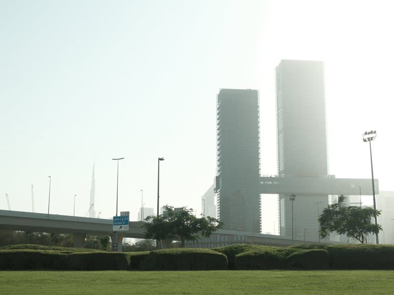 Two tall buildings shrouded in fog with a highway and greenery in the foreground.