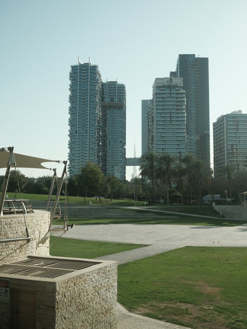 View of modern skyscrapers with a green park in the foreground under clear skies.