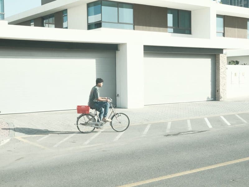A person riding a bicycle on a quiet street beside modern buildings with garage doors.