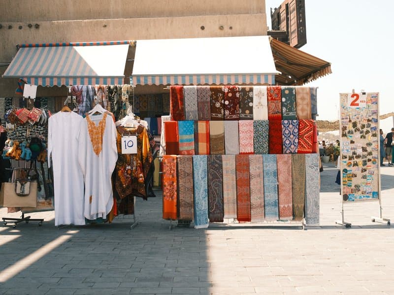 A vibrant market stall displaying colorful textiles and traditional garments under a sunny sky.