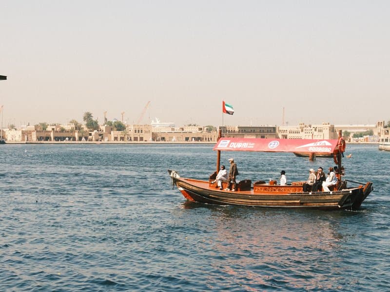 A traditional wooden boat sailing on blue water with a city skyline in the background.