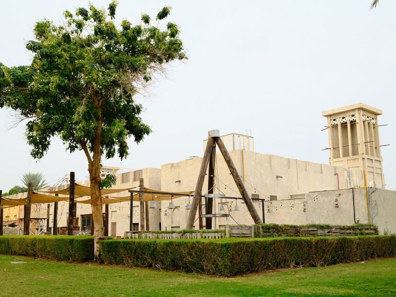 A traditional building with a wind tower, surrounded by greenery and a swing set in a park.