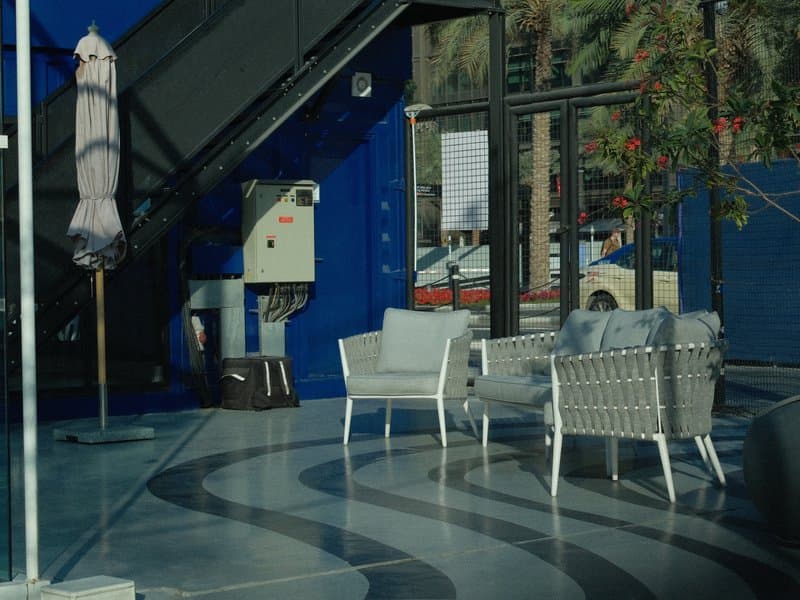 A modern indoor seating area with white chairs and a blue wall, featuring reflections and natural light.