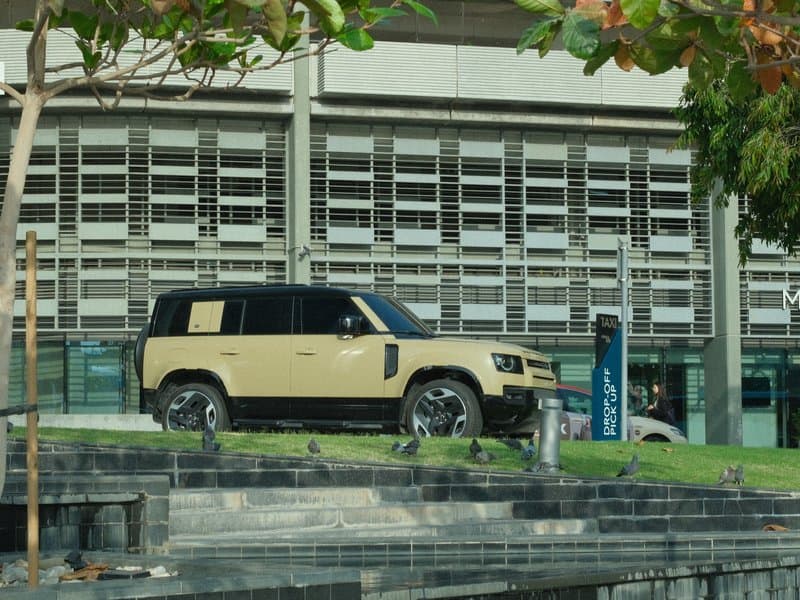 A beige SUV parked on a grassy area next to a modern building with large windows.