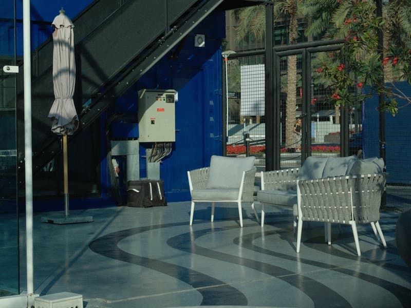 A modern indoor seating area with white wicker chairs and a blue wall, reflecting light and greenery.