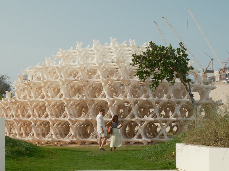 Two people standing near a large, intricate architectural structure made of interconnected shapes.