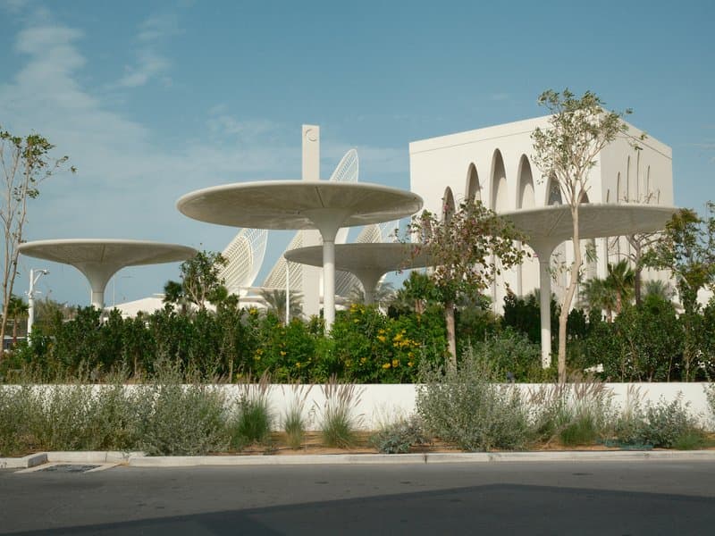 Modern architectural building surrounded by unique umbrella-like structures and greenery.