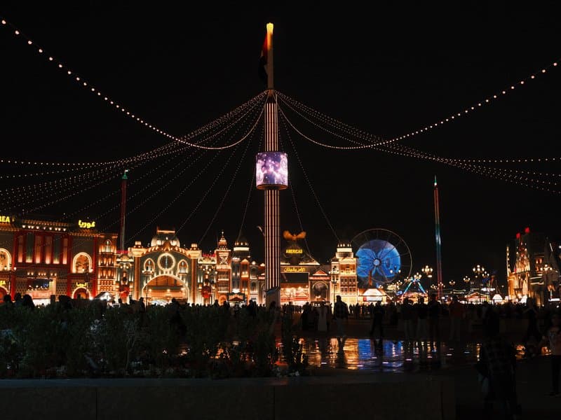 Night view of a vibrant amusement park with illuminated buildings and a ferris wheel.