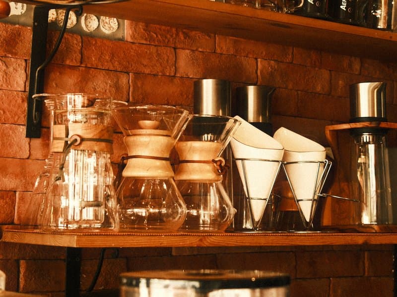 A collection of coffee brewing equipment on wooden shelves against a brick wall.