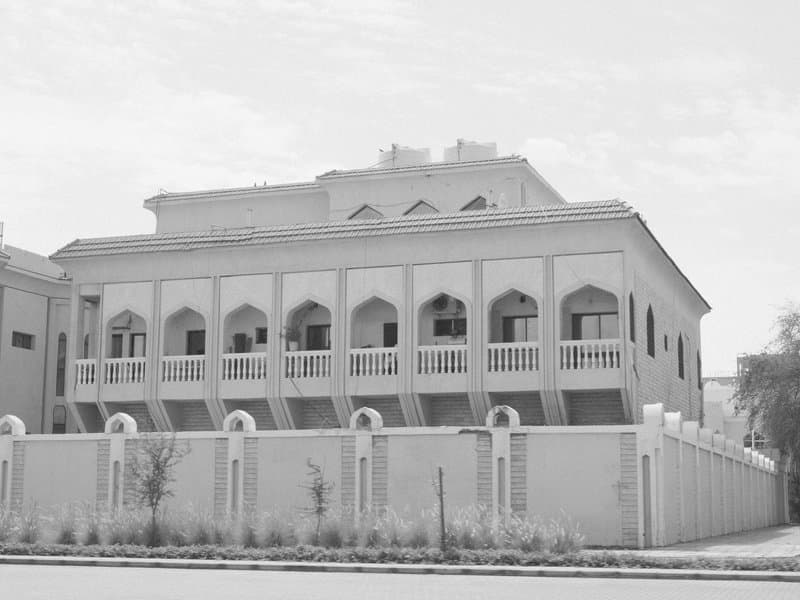 A large, traditional building with arched windows and a decorative facade, surrounded by a low wall.