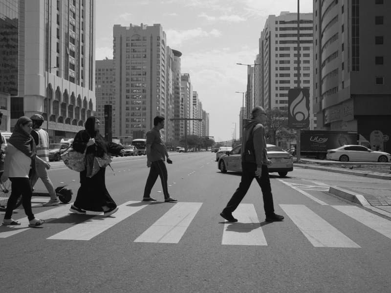 A group of people crossing a street at a crosswalk in a city with tall buildings in the background.