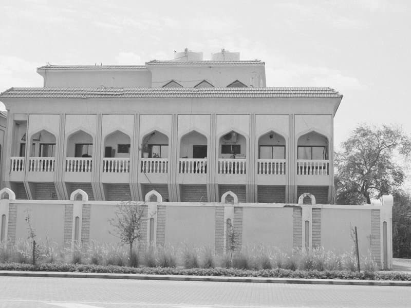 A large, ornate building with arched windows and a decorative facade, surrounded by a low wall.