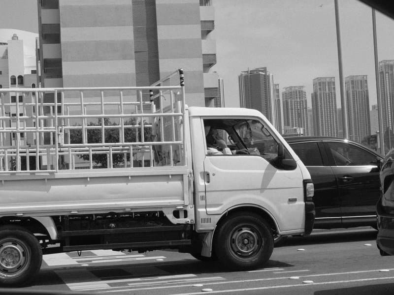 A white truck with a metal cage driving through an urban area with tall buildings in the background.