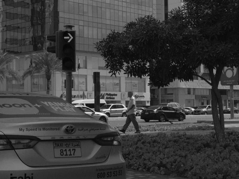 A busy urban street scene with a taxi in the foreground and pedestrians crossing in the background.