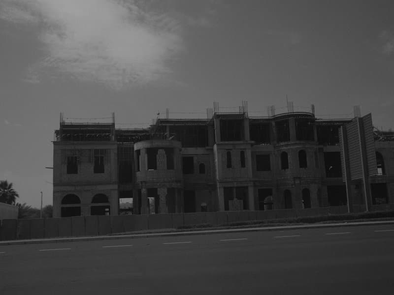 A partially constructed building with a cloudy sky in the background, viewed from the street.